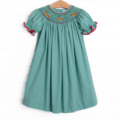  This dress features a green gingham print, puff sleeves, and a reindeer smockings. 