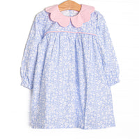 This dress features a blue floral print, a pink scalloped collar, and pink piping