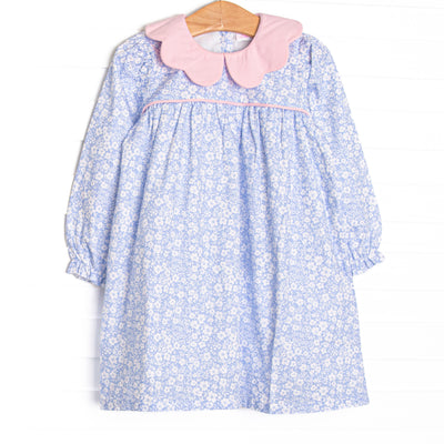 This dress features a blue floral print, a pink scalloped collar, and pink piping