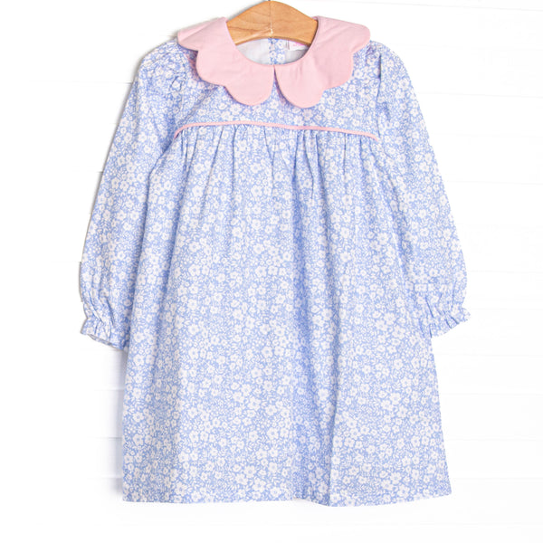 This dress features a blue floral print, a pink scalloped collar, and pink piping