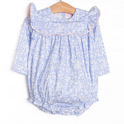  This bubble features a blue floral print, a ruffle bib with pink trim, and snaps on the stride. 