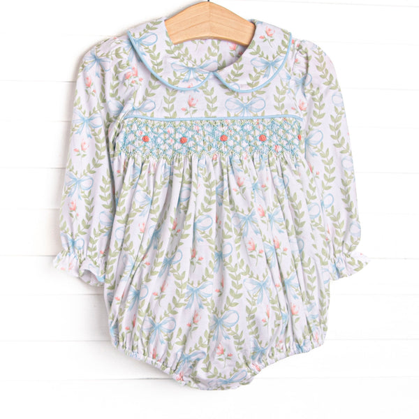 his bubble features a blue floral print, a Peter Pan collar, and a dainty rose smocking. 