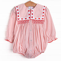  This bubble features pink gingham print, a bib collar with heart embroideries, and a dainty red smocking. 