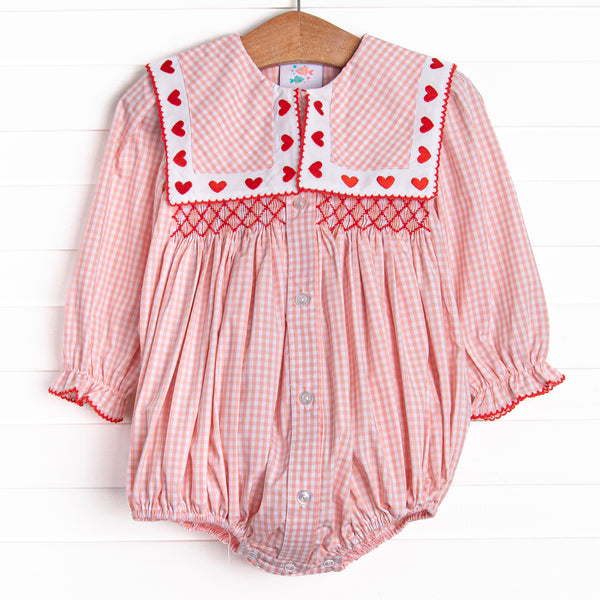 This bubble features pink gingham print, a bib collar with heart embroideries, and a dainty red smocking. 