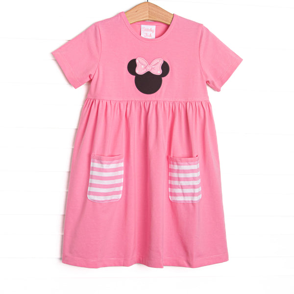  A bright pop of pink, coupled with pink and white striped pockets has us ready for a magical adventure. A mouse ears applique with a whimsical polka dot bow adorns the front of this dress. 