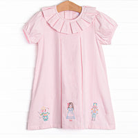  This dress features a pink corduroy material, a ruffle collar, and a nutcracker embroidery. 