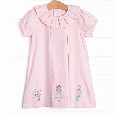  This dress features a pink corduroy material, a ruffle collar, and a nutcracker embroidery. 