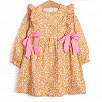  This dress features a yellow floral print, ruffle trim, and pink bows on the sides. 