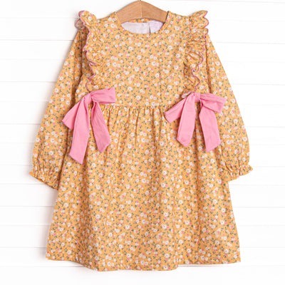  This dress features a yellow floral print, ruffle trim, and pink bows on the sides. 