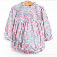  This bubble features a pink floral print, ruffle trim around the neck, and elastic smocking across the chest. 
