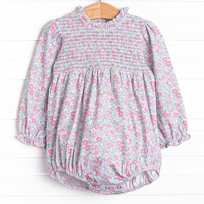  This bubble features a pink floral print, ruffle trim around the neck, and elastic smocking across the chest. 