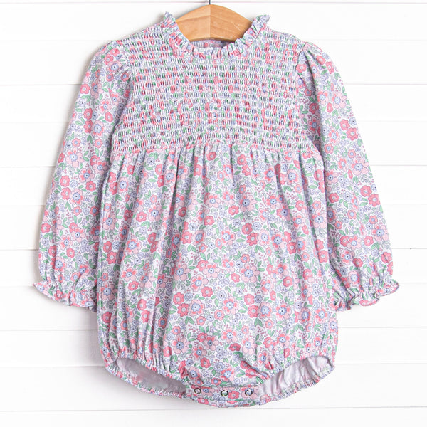  This bubble features a pink floral print, ruffle trim around the neck, and elastic smocking across the chest. 