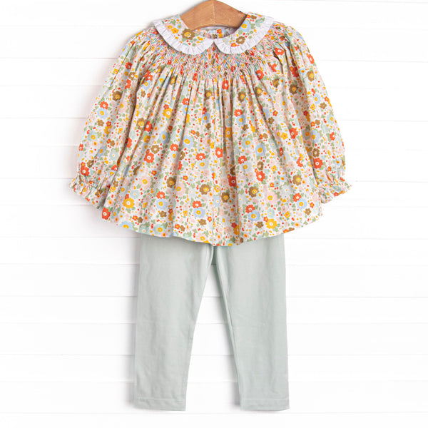 This set features an orange floral print, a peter pan collar with white ruffle trim, and a dainty smocking. Coordinating green leggings to match.