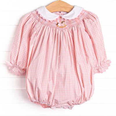 This bubble features a pink gingham print, a peter pan collar with ric rac trim, and a rocking horse smocking.