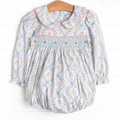  This bubble features a green floral print, a peter pan collar, and a dainty rose smocking. 