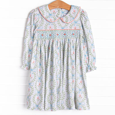 This dress features a green floral print, a peter pan collar, and a dainty rose smocking.