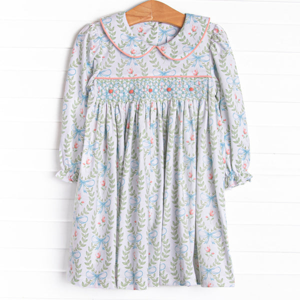 This dress features a green floral print, a peter pan collar, and a dainty rose smocking.