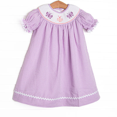 This dress features a purple seersucker print, white ric rac trim, and butterfly smockings