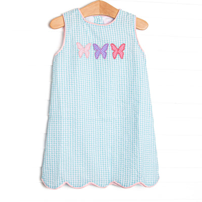 This dress features an mint green gingham print, pink trim, and a trio of butterfly applique.
