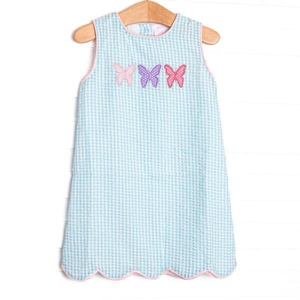 This dress features an mint green gingham print, pink trim, and a trio of butterfly applique.