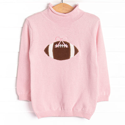 This sweater features a pink material, a rolled neck, and a football icon.