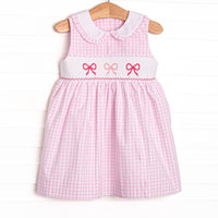 This dress features a pink gingham design, bow smocking, and a ruffle trimmed collar.