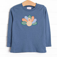  This top features a blue knit material, long sleeves, and a turkey applique. 