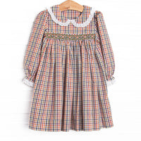 This dress features green plaid printed fabric, dainty smocking, a Peter Pan collar, and white eyelet lace trim.