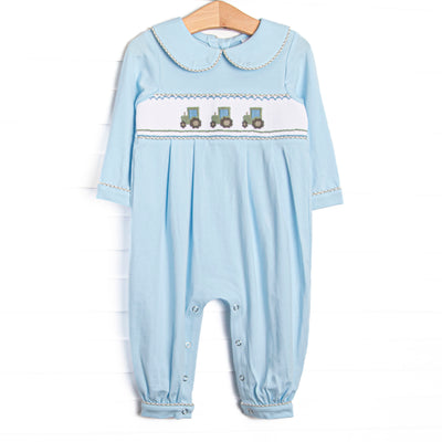 This romper features blue knit fabric, tractor smocking, a blue Peter Pan collar, and snaps along the stride to make changing a breeze.