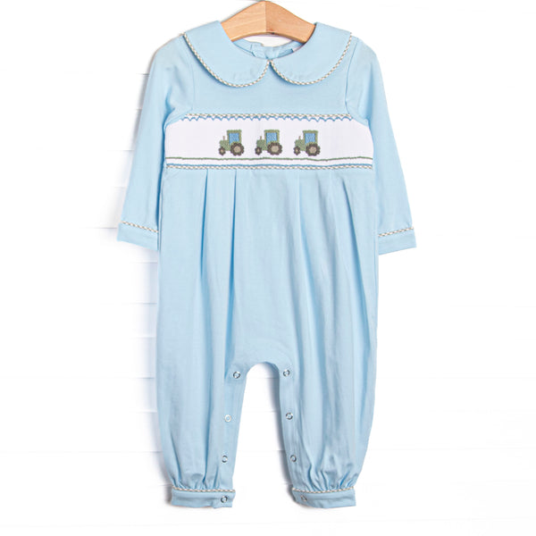 This romper features blue knit fabric, tractor smocking, a blue Peter Pan collar, and snaps along the stride to make changing a breeze.