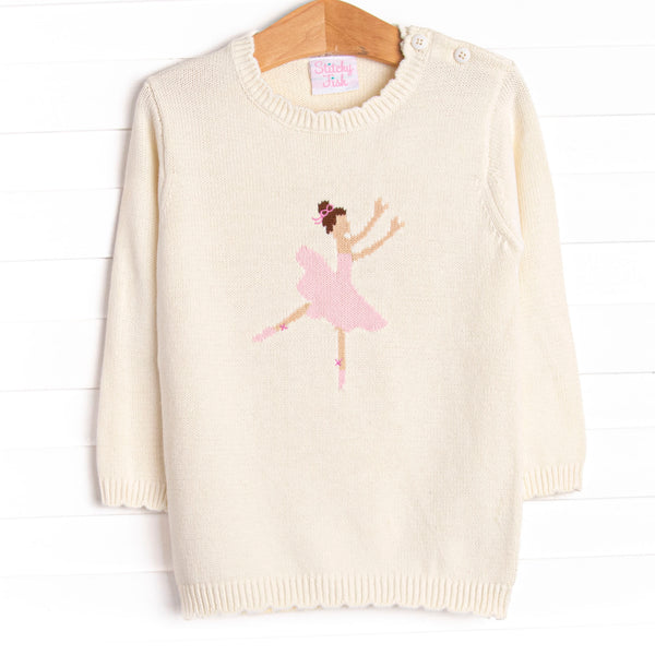  This sweater features a white knit material, buttons on the shoulder, and a ballerina icon. 