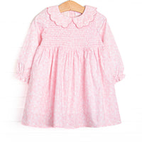 This dress features a pink floral print, a scallop Peter Pan collar, and smocking on the chest.