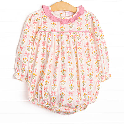 This bubble features pink floral and bow print, a pink ruffle collar, and long sleeves.