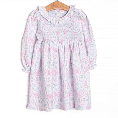  This dress features a floral and bow print, a ruffle collar, and chest smocking. 
