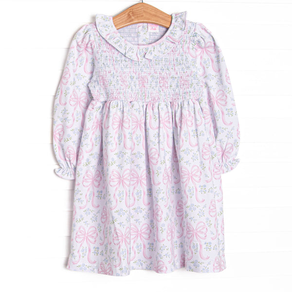  This dress features a floral and bow print, a ruffle collar, and chest smocking. 