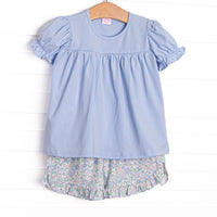  This set features a blue shirt with puff sleeves and blue floral ruffle shorts to match. 