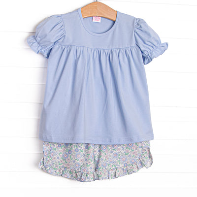  This set features a blue shirt with puff sleeves and blue floral ruffle shorts to match. 