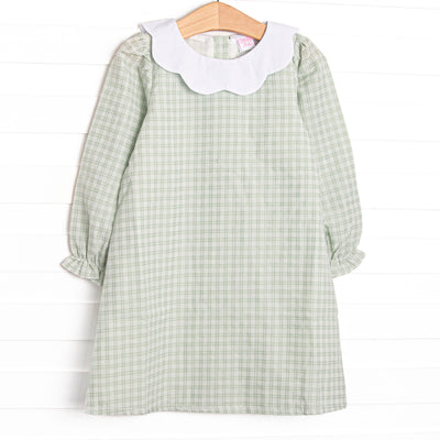 This dress features a green plaid print, a scallop bib collar, and button closure on the back.