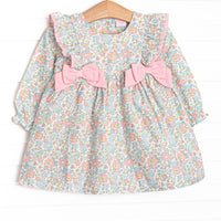 This dress features a pink floral print, ruffle trim, and pink bows.