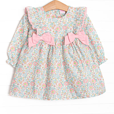 This dress features a pink floral print, ruffle trim, and pink bows.
