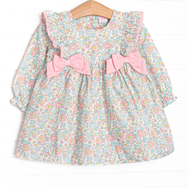 This dress features a pink floral print, ruffle trim, and pink bows.