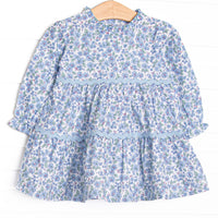 This dress features a blue floral print, tiered ruffles, and ruffles around the neck.