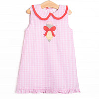  This dress features a pink plaid material, a Peter Pan collar with red ruffle trim, a ruffle bottom edge, and a pencil bow applique. 