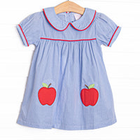  This dress features a blue mini gingham fabric, a Peter Pan collar with red piping, and apple appliques. 