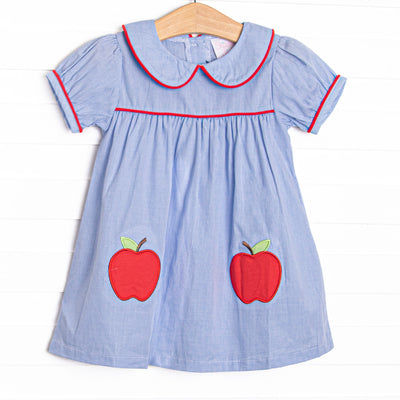  This dress features a blue mini gingham fabric, a Peter Pan collar with red piping, and apple appliques. 