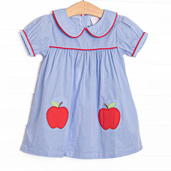  This dress features a blue mini gingham fabric, a Peter Pan collar with red piping, and apple appliques. 