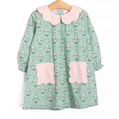 This dress features a tile and floral print, a pink scalloped collar, and pink scalloped front pockets.