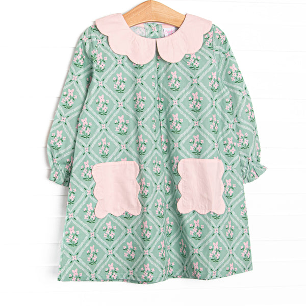 This dress features a tile and floral print, a pink scalloped collar, and pink scalloped front pockets.