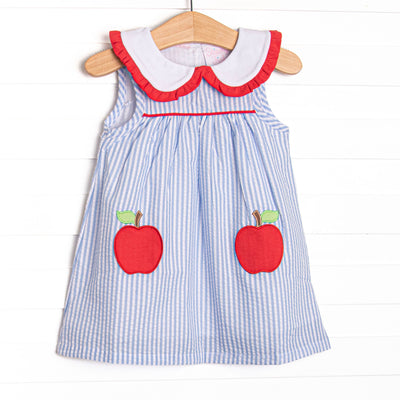 This dress features a blue seersucker print, a peter pan collar with red ruffles, and an apple applique.