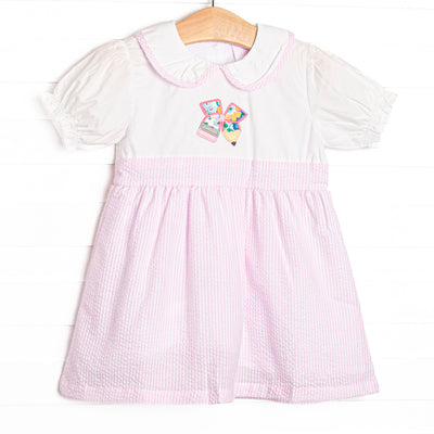  This dress features a pink seersucker material, a Peter Pan collar with pink seersucker trim, and a pencil petal applique. 